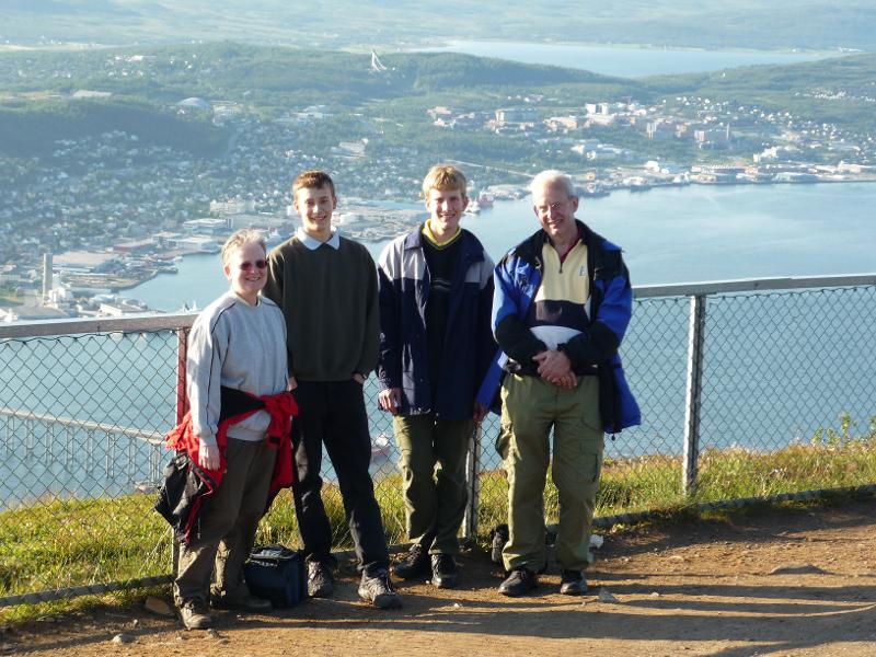 Familiefoto p&aring; en h&oslash;yde med en by i bakgrunnen. To br&oslash;dre med sine foreldre. 